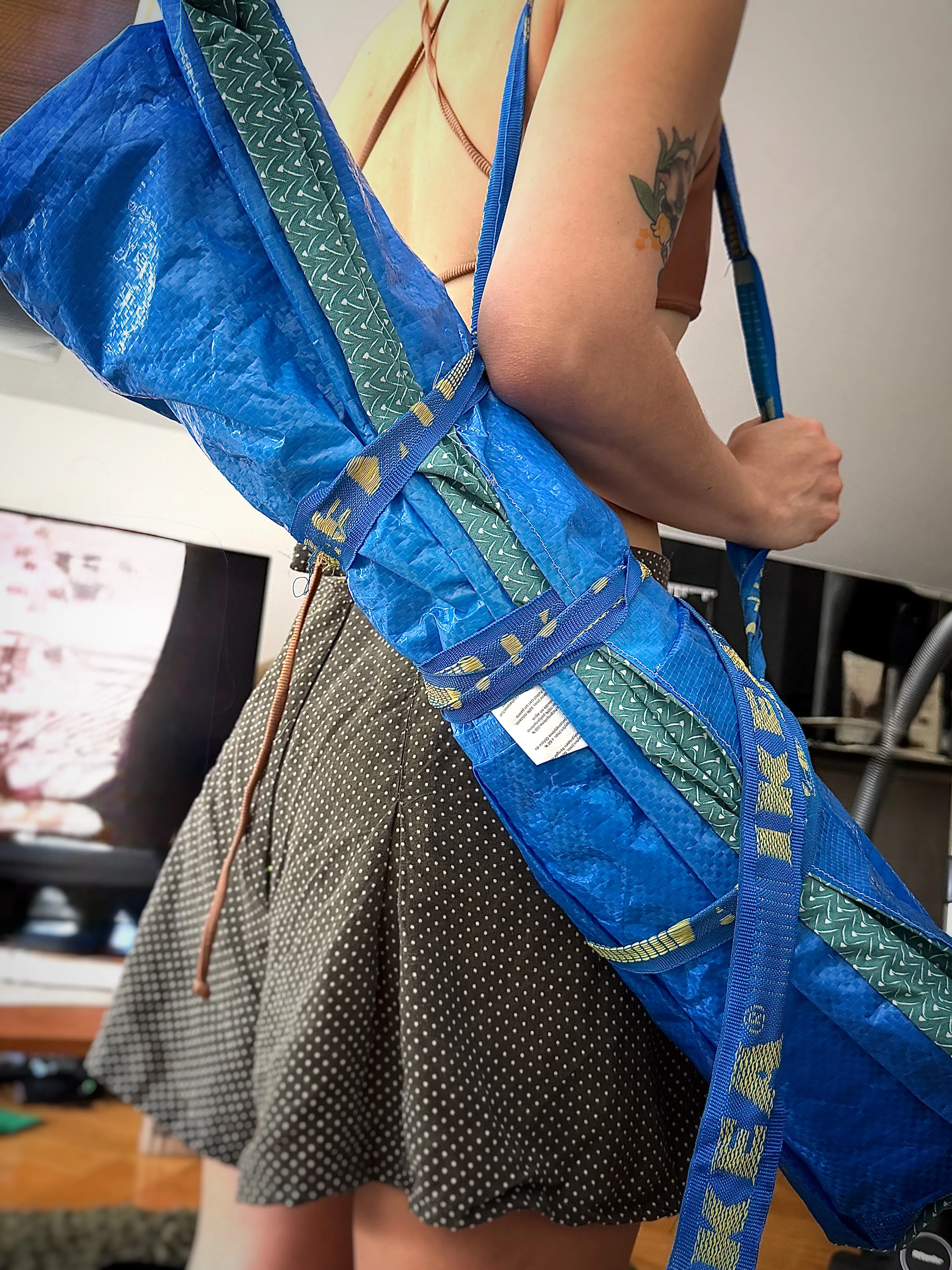 rolled-up picnic blanket in blue IKEA Frakta fabric, slung across the back like a yoga-mat carrier by its yellow straps