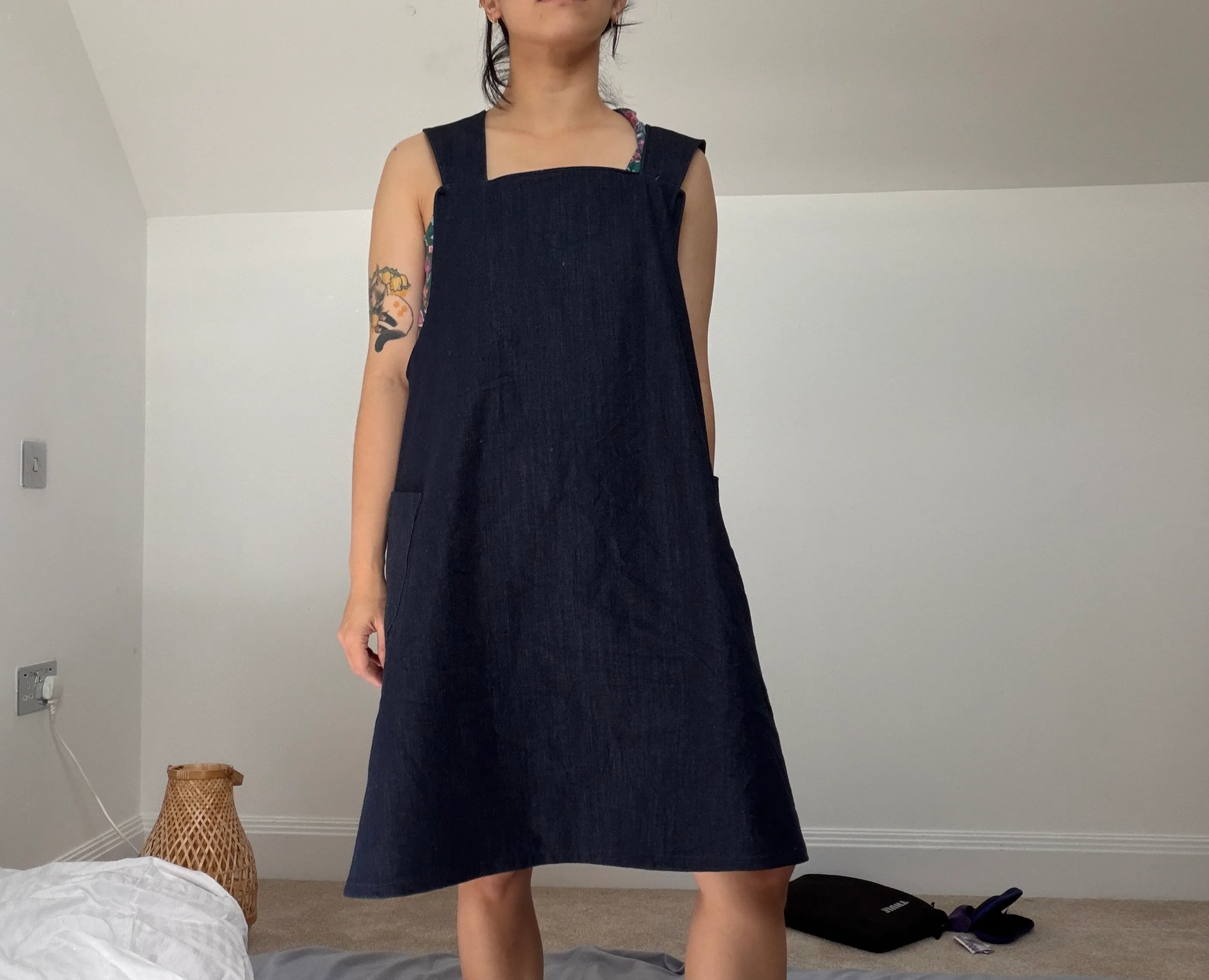 Front view of the finished navy denim pinafore, square neckline and A-line shape, worn over a floral top