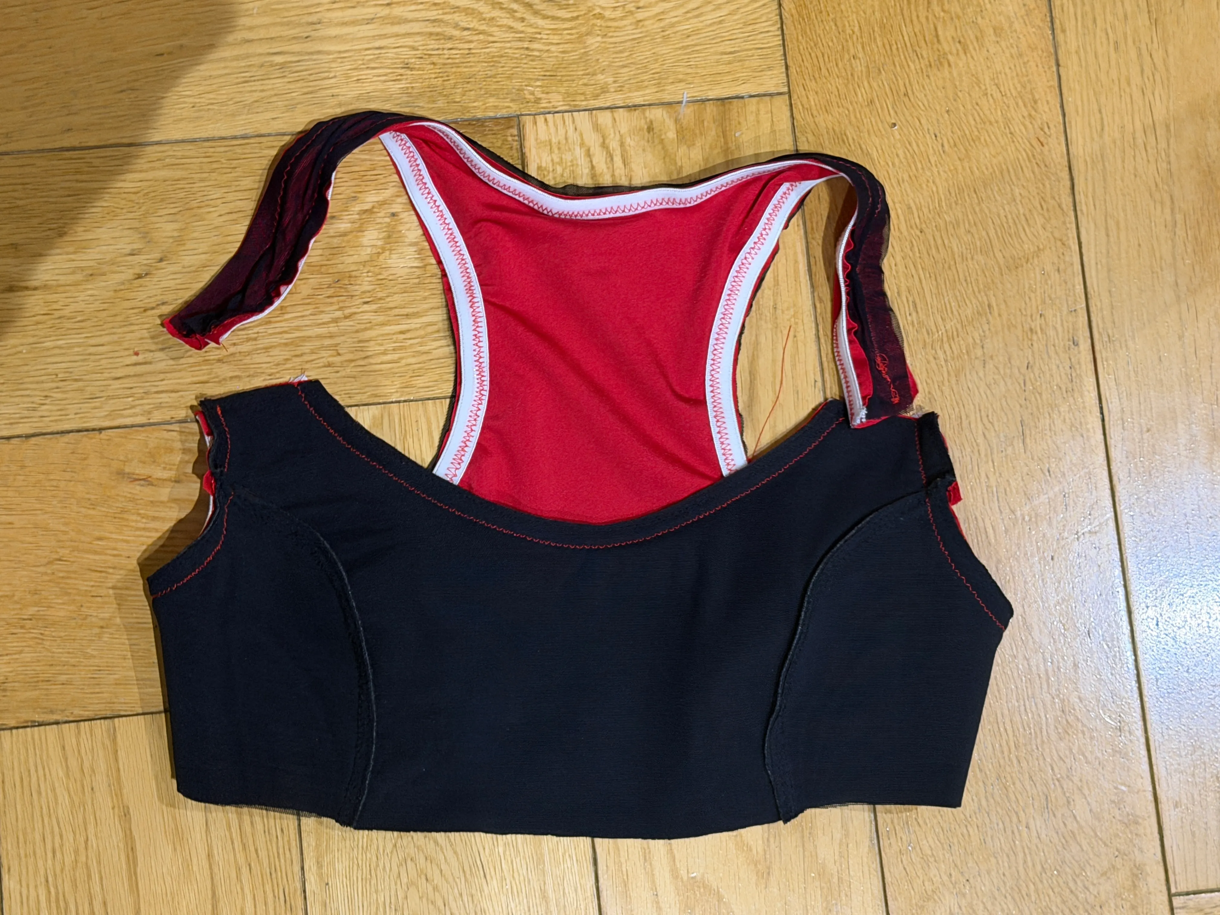 Back view of the finished racerback bra on a wood floor — black outer, red lining, white elastic binding